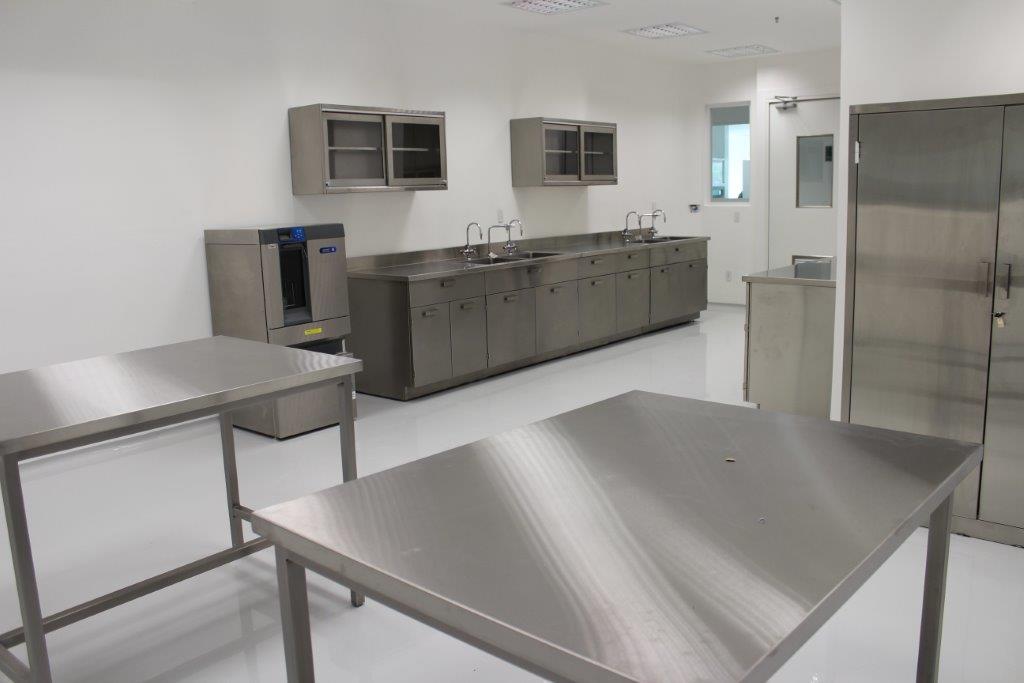 Laboratorio farmacéutico con mesas y gabinetes de acero inoxidable grado sanitario, demostrando un ambiente estéril.