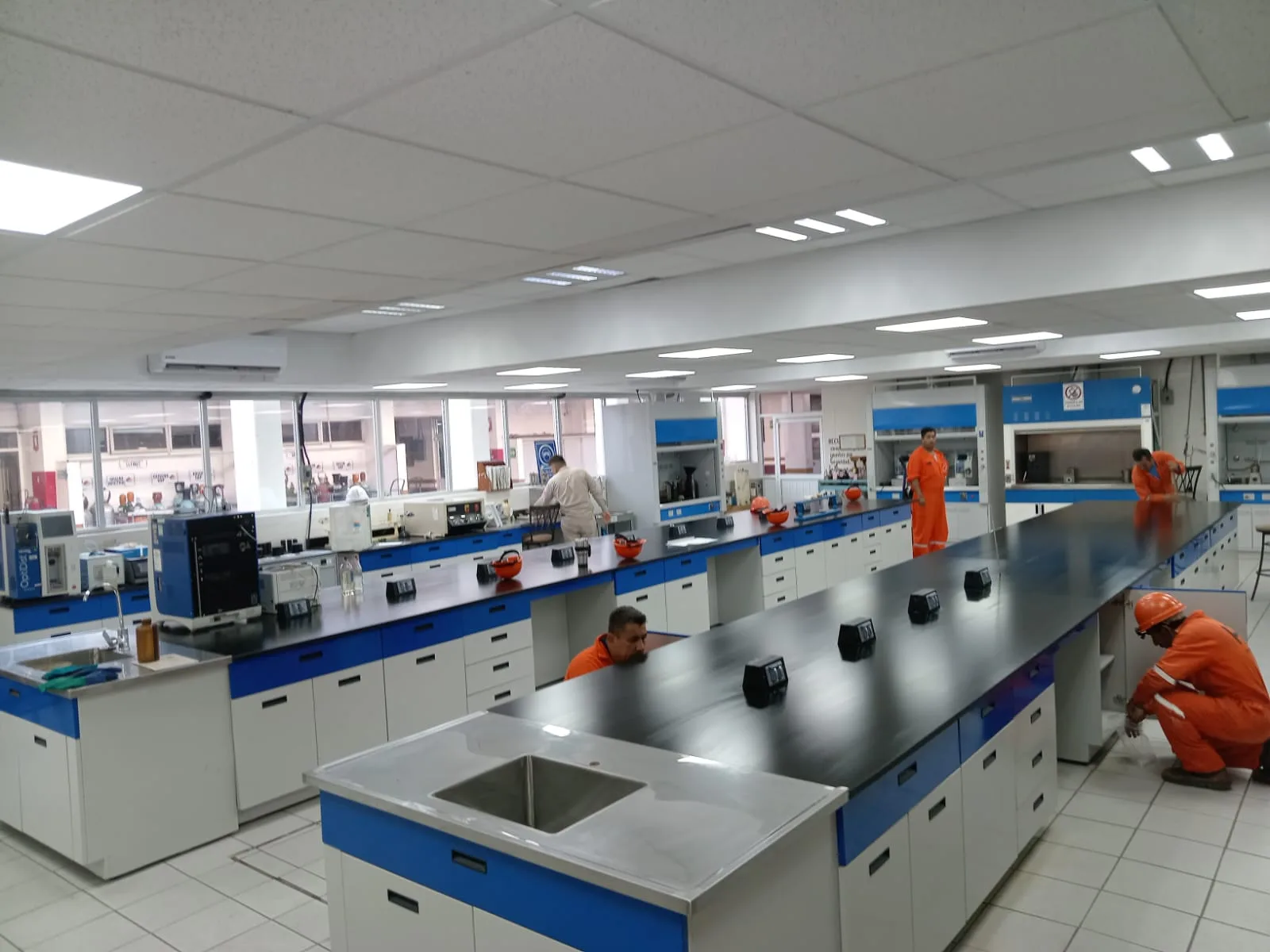 Laboratorio Pemex: sala amplia con mesadas paralelas y personal en área industrial